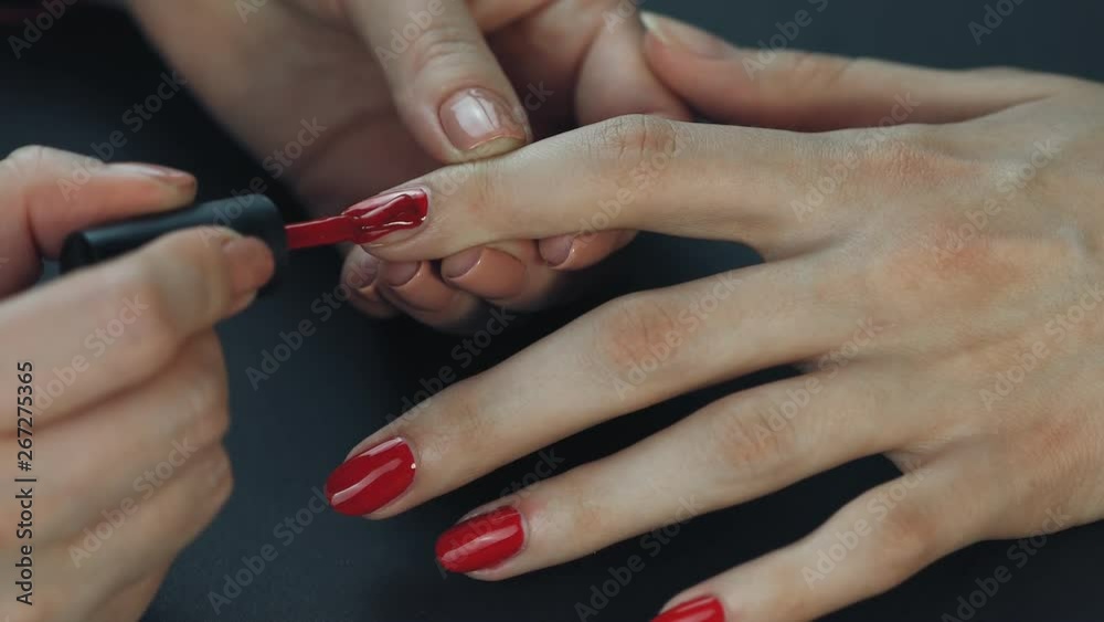 the manicurist paints the client's nails with red nail polish on a black background Painting nails. the manicurist paints the client's nails with red nail polish on a black background Painting nails.