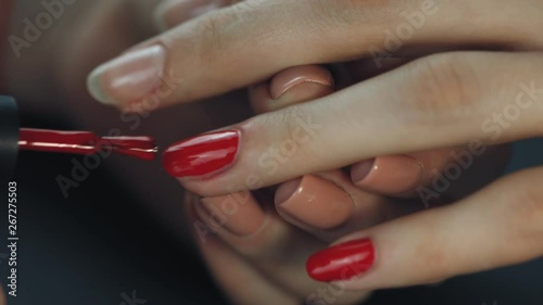 the manicurist paints the client's nails with red nail polish on a black background Painting nails.