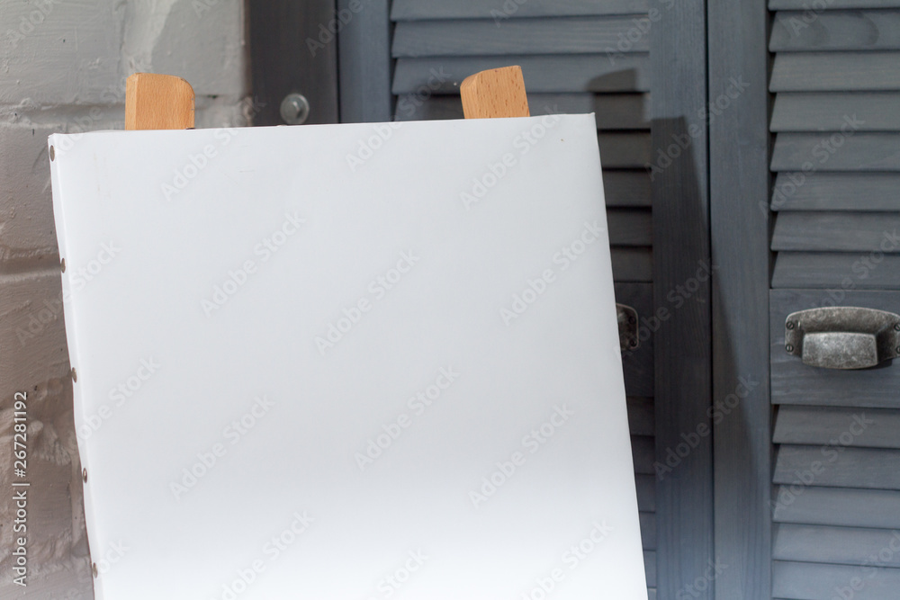 An easel with a clean white canvas is ready for work against a white brick wall, background or concept An easel with a clean white canvas is ready for work against a white brick wall, background or concept