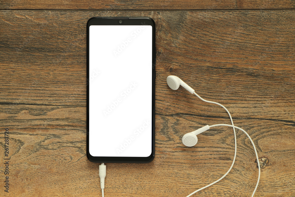 Smartphone with isolated white blank screen with connected earphones on the background of a wooden desk Smartphone with isolated white blank screen with connected earphones on the background of a wooden desk