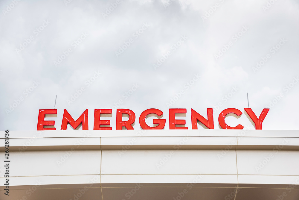 Obraz premium A prominent red 3D all-caps lighted emergency directional sign and marker perched on the awning and canopy of the main hospital entrance.