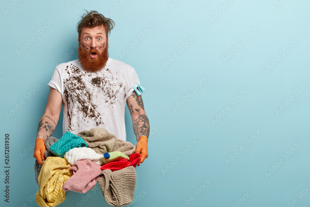 Horizontal shot of stupefied housekeeper carries laundry basket, has