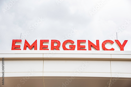 A prominent red 3D all-caps lighted emergency directional sign and marker perched on the awning and canopy of the main hospital entrance.