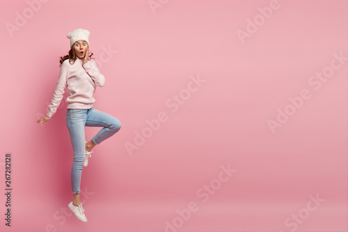 Tableau sur toile Stupefied young European woman with curly hair, wears stylish clothing, jumps hi
