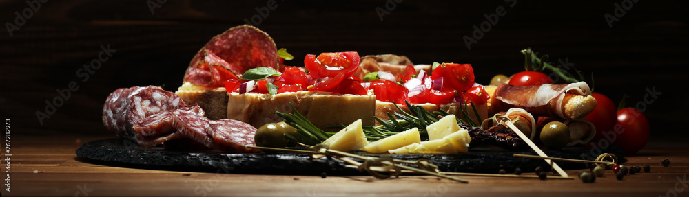Traditional italian antipasto bruschetta appetizer with cherry tomatoes, cream cheese, basil leaves and balsamic vinegar on cutting board with prosciutto, salami, cheese Traditional italian antipasto bruschetta appetizer with cherry tomatoes, cream cheese, basil leaves and balsamic vinegar on cutting board with prosciutto, salami, cheese