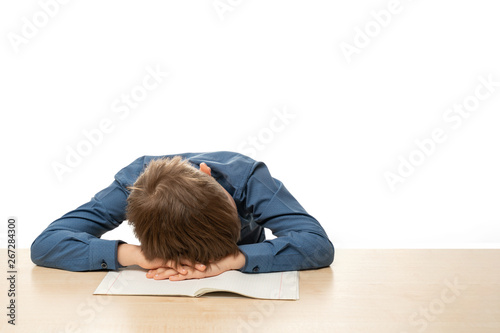 A teenager in a blue shirt fell asleep at a table in class. Isolate on white background.