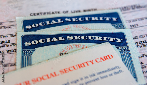 wo USA Social Security cards with number obscured surrounded by US dollars or American dollars.  The SSN has become a de facto national identification number for taxation and other purposes.