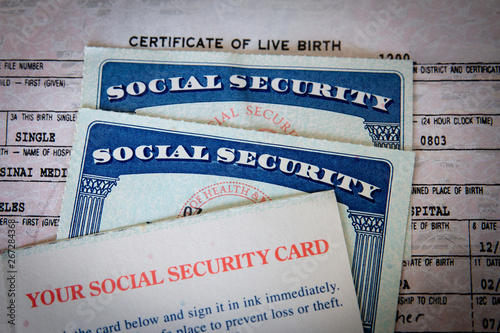 wo USA Social Security cards with number obscured surrounded by US dollars or American dollars.  The SSN has become a de facto national identification number for taxation and other purposes.