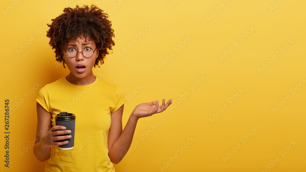 Αυτοκόλλητο Horizontal studio shot of indignant woman raises hand, looks with puzzled expression, has talk with interlocutor during coffee break, holds paper cup, frustrated by latest bad news