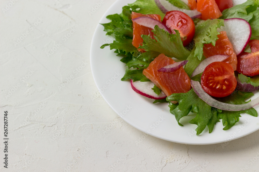 Fresh salad from salmon and vegetables on a white plate.