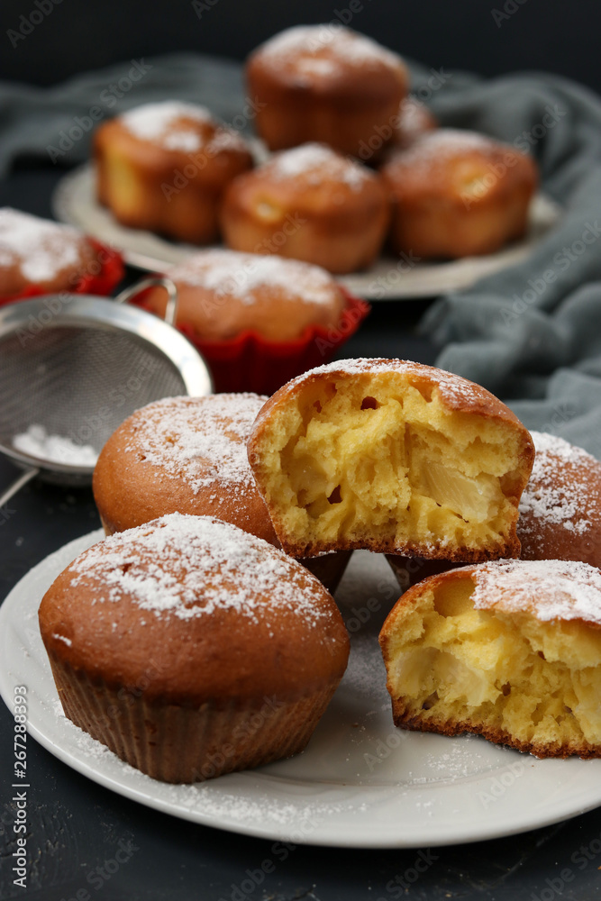 Homemade muffins with pineapple pieces, sprinkled with powdered sugar, are located on a dark background