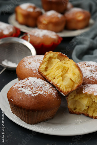 Homemade muffins with pineapple pieces, sprinkled with powdered sugar, are located on a dark background