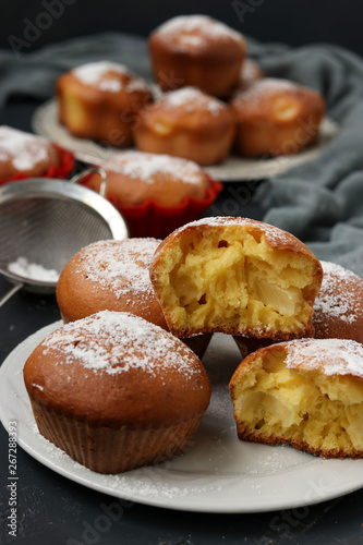 Homemade muffins with pineapple pieces, sprinkled with powdered sugar, are located on a dark background