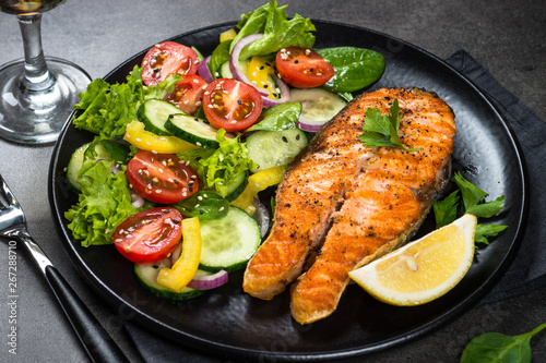 Grilled salmon fish steak with vegetables on black.