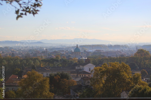 Lucca, Italy: View from the top of the Guinigi Tower to the far rooftops of the city and surrounding mountains through transparent blue haze