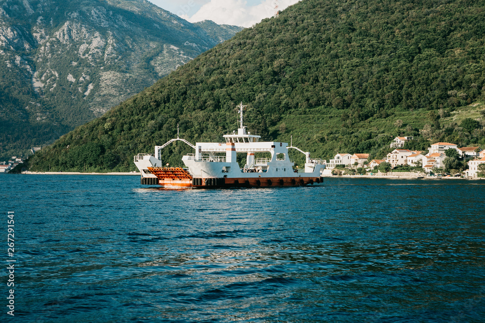 A ferry to transport vehicles and people crosses the bay in Montenegro and approaches the city.