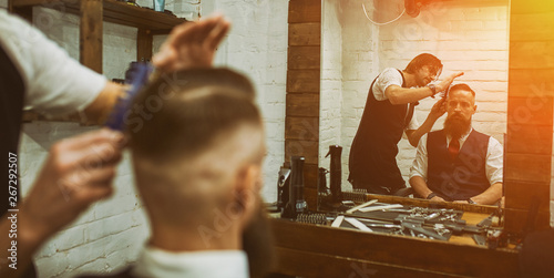 Master cuts hair and beard of men in the barbershop, hairdresser makes hairstyle for a young man