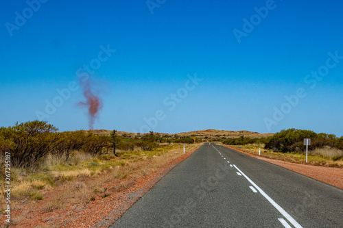 Dust devil besides dark road leading through red sanded Australian landscape towards Karijini National Park photo
