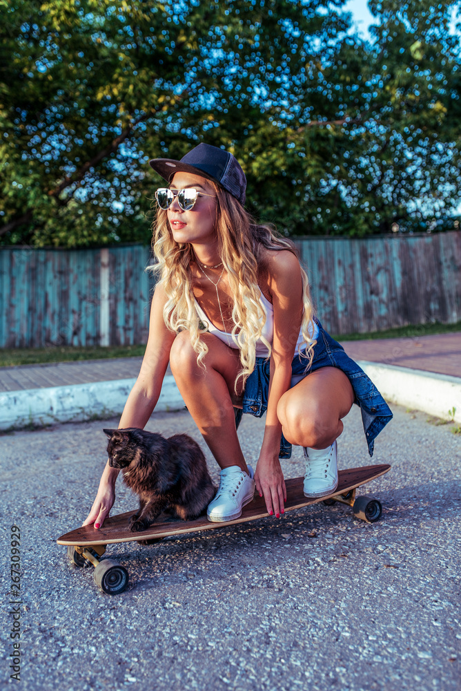 Woman on skate, cat pet pussy, summer in city, background fence road. Denim baseball  cap long