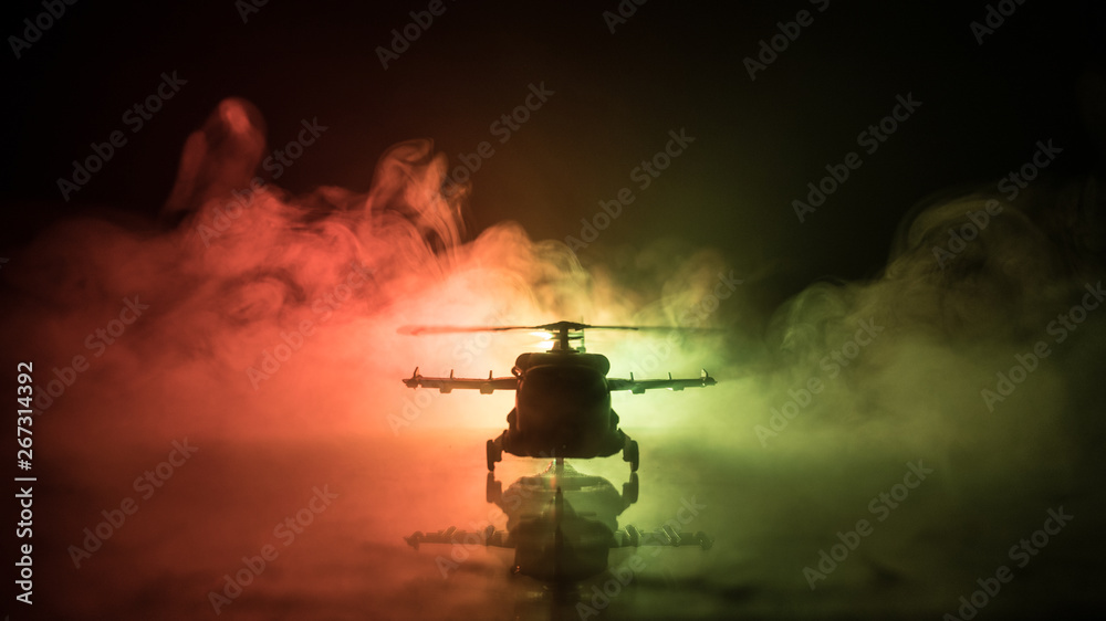 Naklejka premium Silhouette of military helicopter ready to fly from conflict zone. Decorated night footage with helicopter starting in desert with foggy toned backlit. Selective focus.
