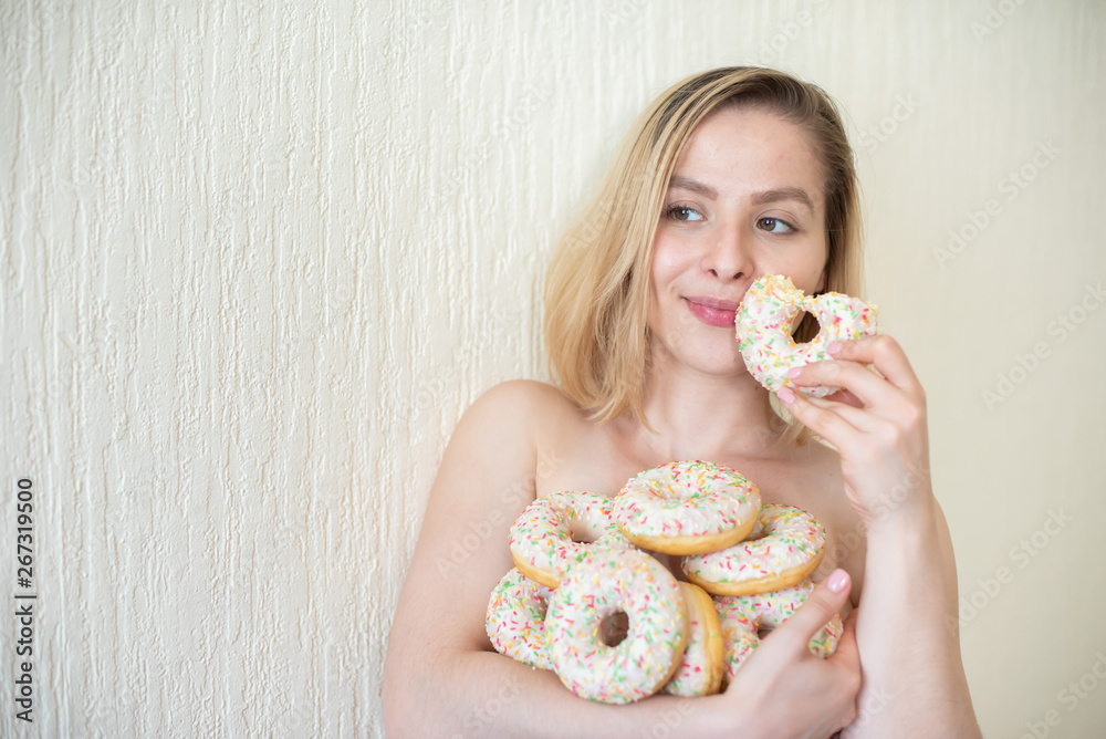 Nude young woman eating donuts. Portrait of an attractive woman with a