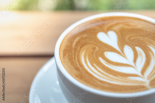 Food, Drink and Relaxation concept. Close up of white cup of hot coffee latte with milk foam heart shape art.