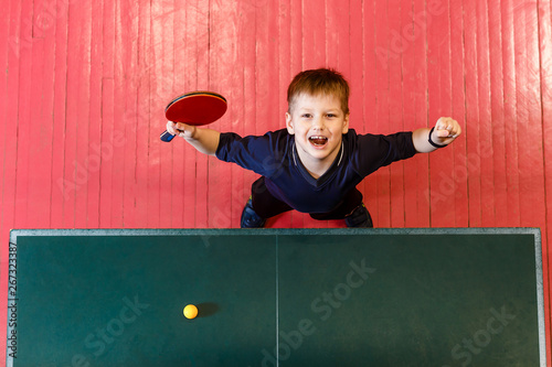 cheerful seven-year-old child enjoys winning table tennis, top view.