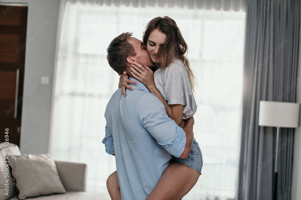 Young beautiful romantic couple in love kissing and carrying embracing at home - obrazy, fototapety, plakaty 