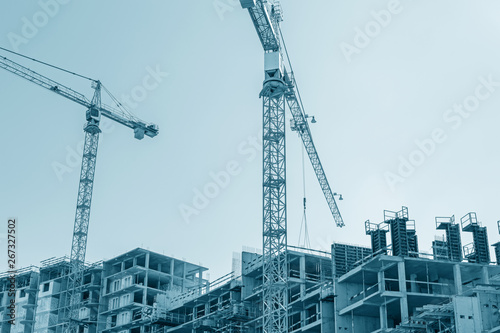 modern city building under construction and yellow cranes against blue sky background