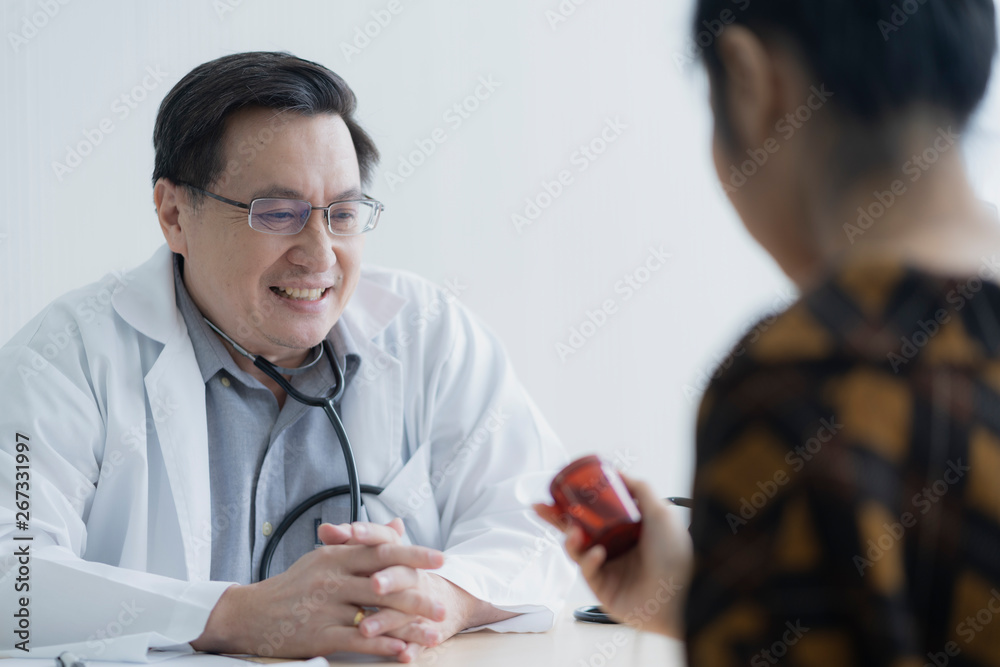 The senior male doctor talked and handed the red pill jar to the patient at the doctor's room. The senior male doctor talked and handed the red pill jar to the patient at the doctor's room.