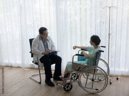 The senior male doctor talked and inquired about the patient s illness at the wheelchair of the patient.