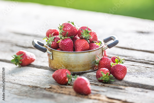 Fresh ripe strawberries in vintage kitchen pot on old garden table