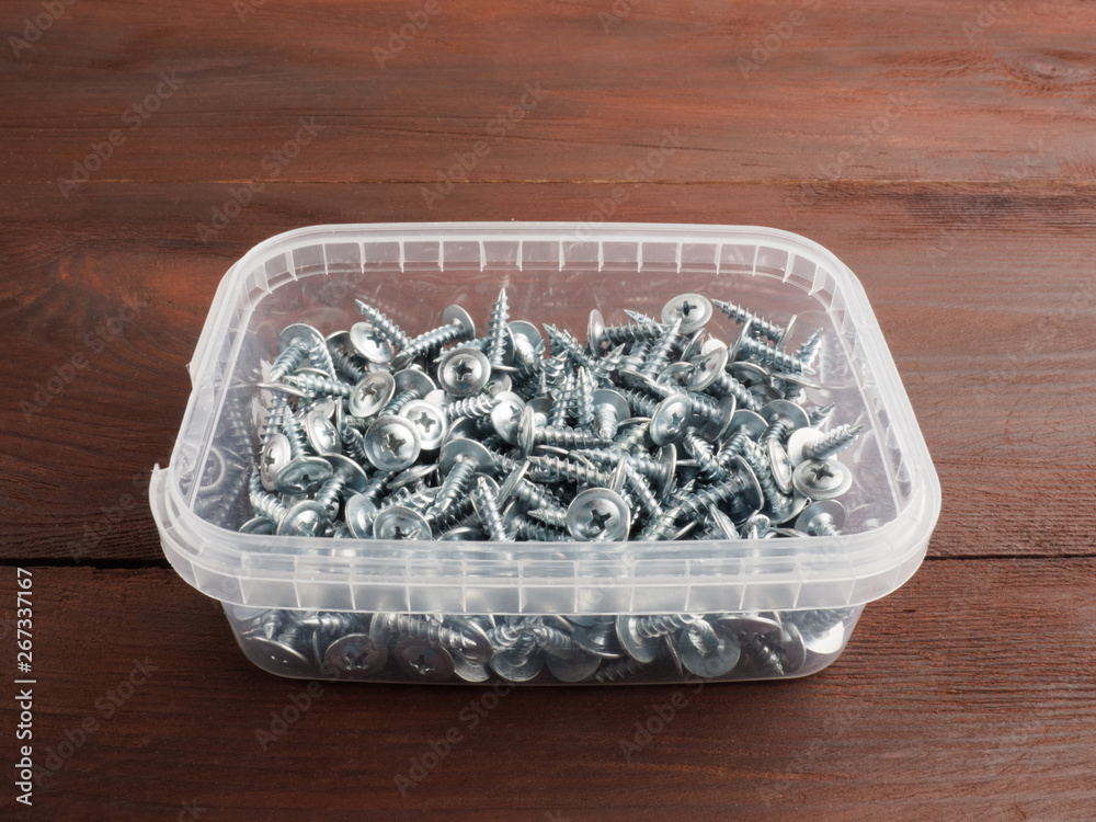 Fototapeta premium Group of silver color steel screws in box, on brown background. Industrial theme