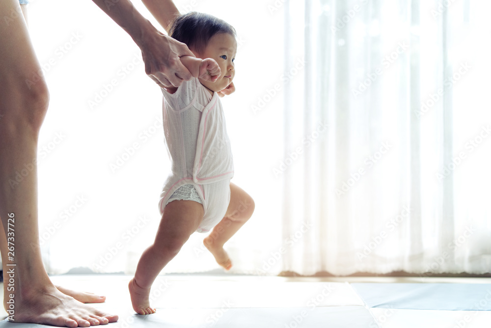 Asian baby taking first steps walk forward on the soft mat. Happy little  baby learning to