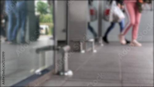 Many people visitors of mall walk through the glass door for shopping. Legs close-up, bottom view. Blurred frame.