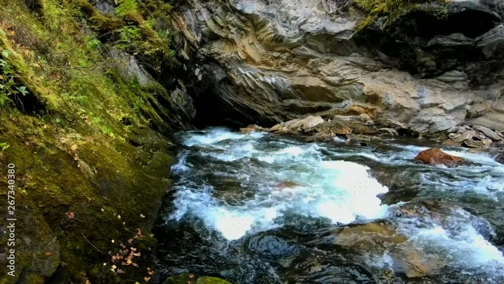 Wild stream flows into a small dark cave in a rocky mountain Wild stream flows into a small dark cave in a rocky mountain