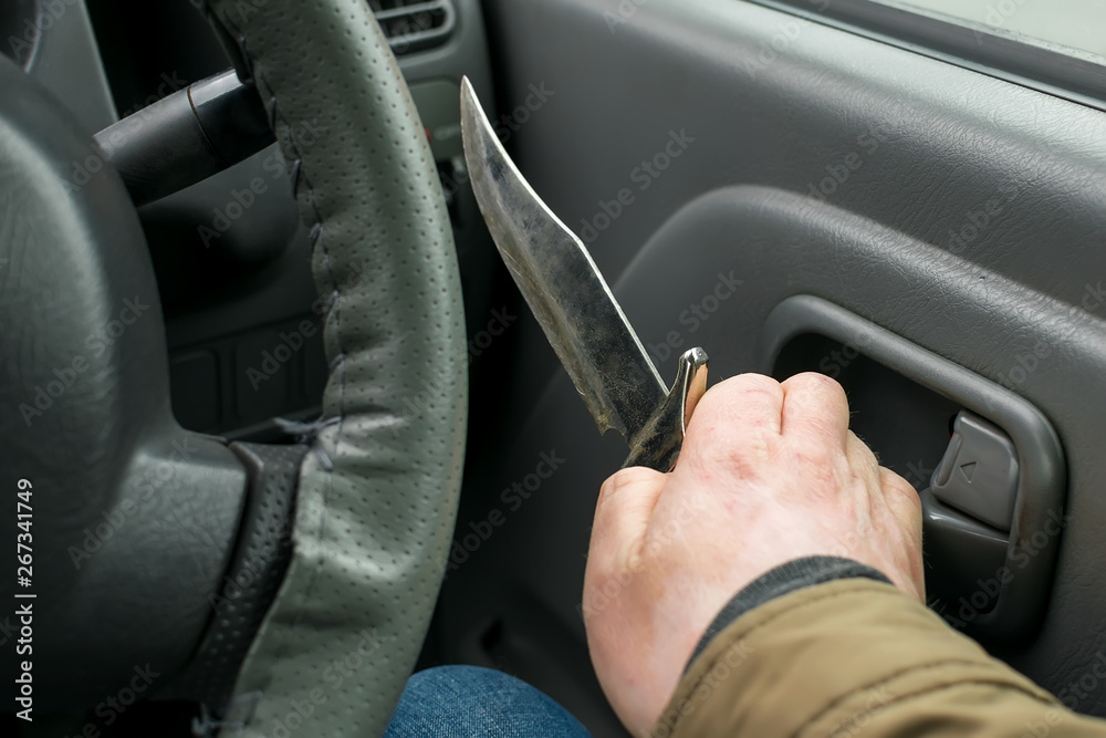 View of the knife in the hand of the driver inside the car, which is going to open the door