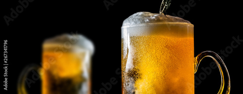 Two large glasses of beer with foam close-up, facing each other, isolated against a black background. Two overflowing glasses of beer with flowing foam.