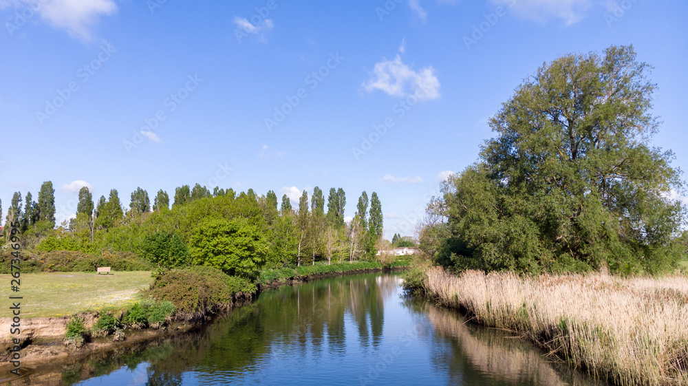 An aerial view of a river with trees on the bank along a park under a majestic blue sky and white clouds An aerial view of a river with trees on the bank along a park under a majestic blue sky and white clouds