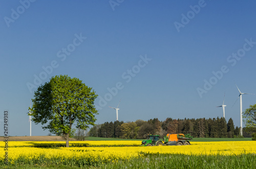 COUNTRY ROAD AND WIND FARM - Agricultural machine among spring rape fields