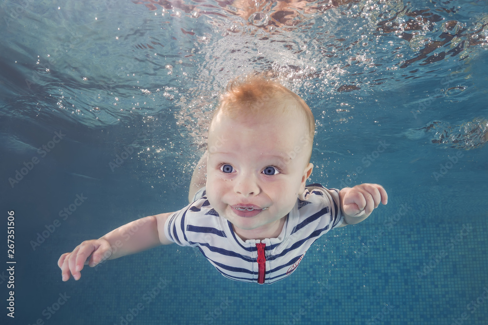 Little baby boy in a striped suit learns to swims underwater in the swimming pool. Healthy family lifestyle and children water sports activity. Child development, disease prevention