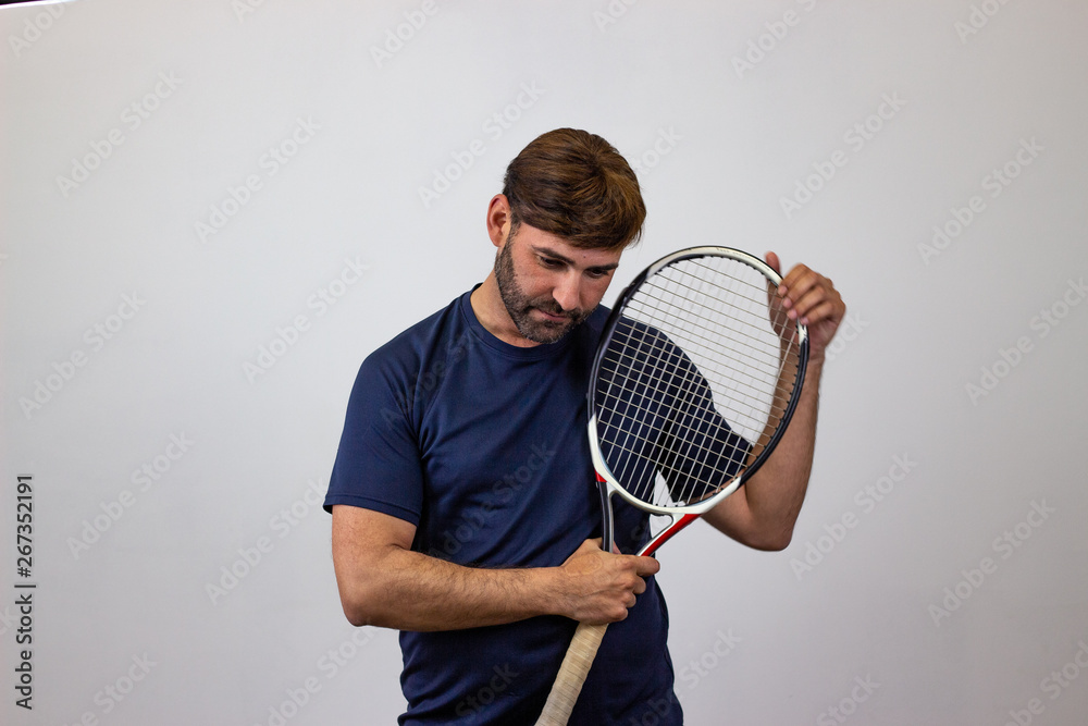 Portrait of handsome young man playing tennis holding a racket with brown hair bored, looking at the camera. Isolated on white background.
