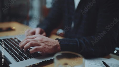 Hipster sitting with laptop and working at loft. Man wearing eye glasses and typing laptop keyboard at office