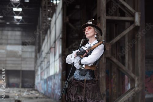 elderly lady in a steampunk costume at an abandoned factory with arms in hand