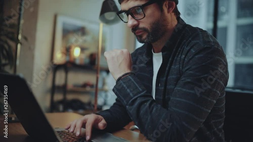 Bearded hipster man wearing eye glasses and using devices at office.Confident busy male freelancer in trendy eyewear using laptop while surfing net searching information for presentation
