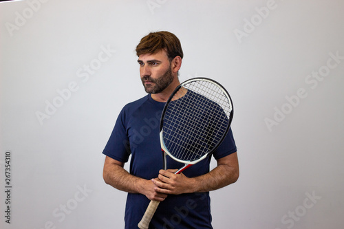 Portrait of handsome young man playing tennis holding a racket with brown hair showing bad face, facing forwards and looking at the horizon. Isolated on white background. © Sergio Barceló