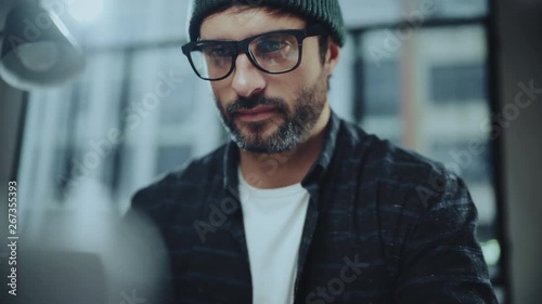 Bearded hipster man wearing eye glasses and using devices at office.Confident busy male freelancer in trendy eyewear using laptop while surfing net searching information for presentation