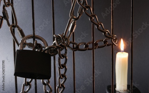 Metal chain, burning candle and padlock on metal fencingn black background