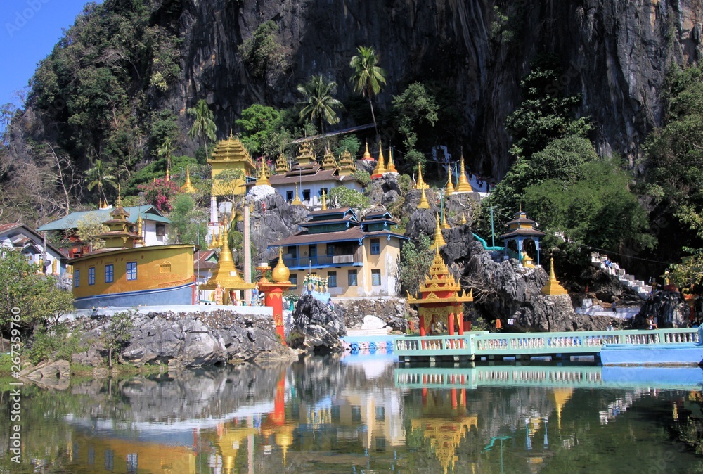 View on colorful kitschy temple with golden towers reflecting in a lake against steep mountain face and bridge - Bayin Nyi Begyinni Pagoda near Hpa An, Myanmar