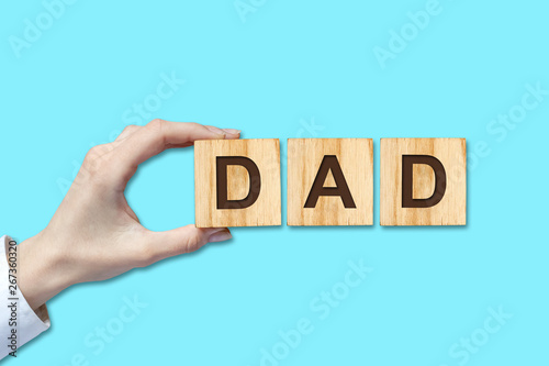 Happy father's day background. Female hand with the word, dad written on wooden blocks. Blue background Congratulatory background.